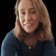 Maria Virgínia1-Photoroom A professional headshot of me smiling at the camera. I have light brown hair, brown eyes, and am wearing a blue shirt with two delicate necklaces—one with a blue heart pendant and the other with a golden heart.