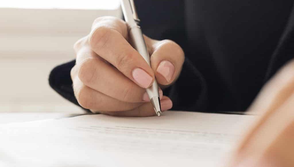 Hand signing a legal document with a pen, representing certified translation for contracts and visa applications